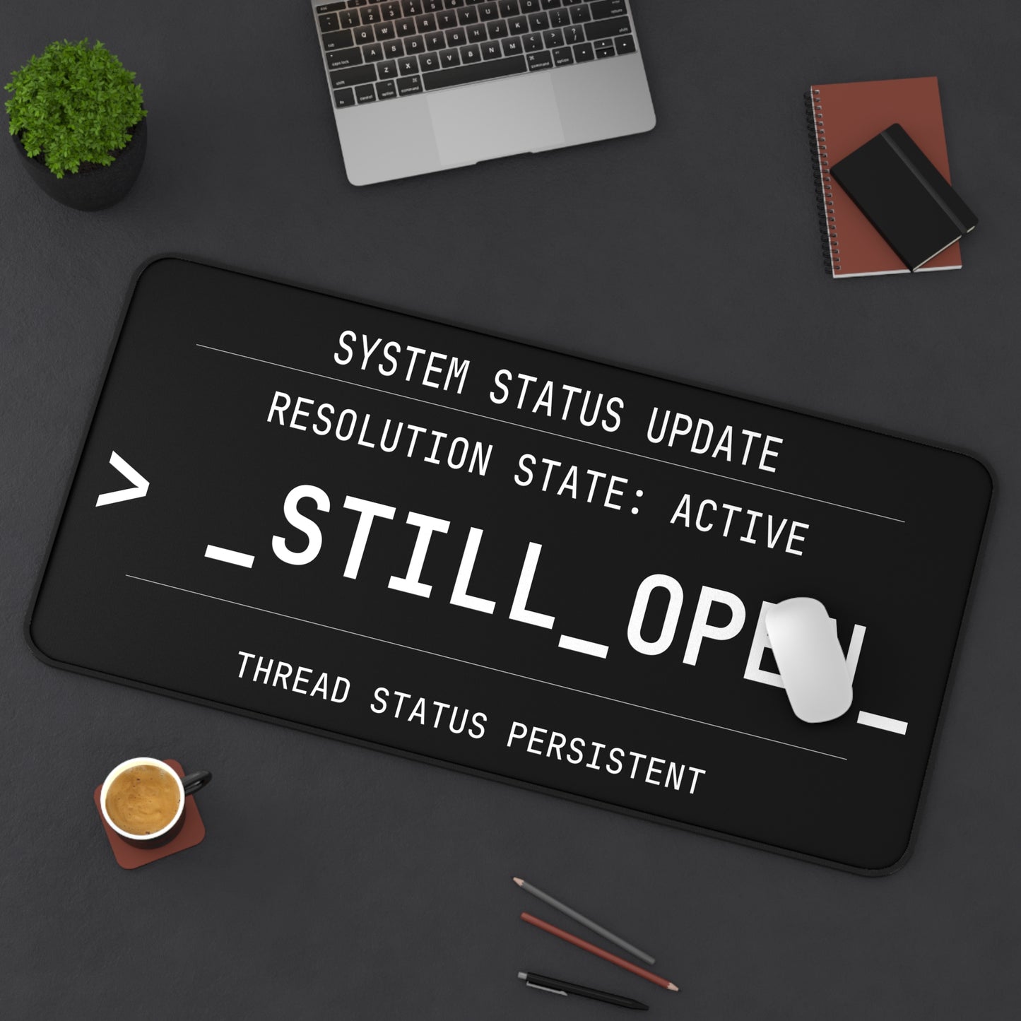 Black desk mat with text design on a dark surface with office items.